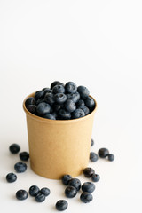 Fresh organic blueberries in a paper cup on a white background.