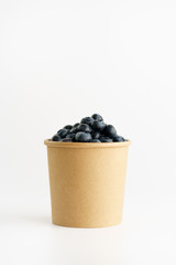 Fresh organic blueberries in a paper cup on a white background.