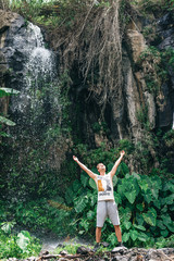 caucasian man with hands up under a waterfall cascade in jungle of Africa