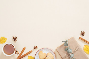 Obraz na płótnie Canvas Flatlay autumn composition. Frame made of cup of tea, autumn dry leaves, cinnamon sticks, cookies, gift box on pastel beige background. Flat lay, top view, copy space. Autumn minimal concept.