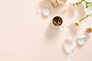 Herbal tea, candles, ribbon, gift box, chamomile flower on pastel pink background. Minimal flat lay style composition, top view, overhead.