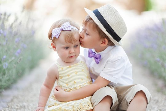 Little brother kisses his sister on the cheek near the blooming lavender. Warm summer. Spring.