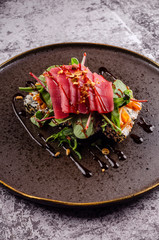 Close up of sashimi sushi set with raw tuna steak, avocado, cucumber and cheese philadelphia and chopsticks on elegant black plate on concrete background. Modern Japanese food menu.
