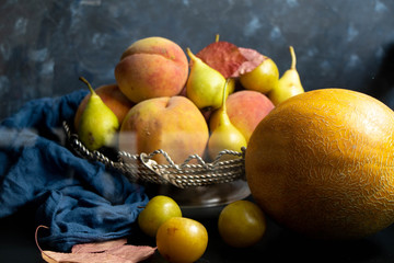 Melon lies on an oval plate, next to it, on a saucer a sliced ​​lobule. Metalic knife, peaches, cloth, dark background. Still life. 