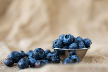 Fresh organic blueberries in a plate of metal on burlap cloth on a rustic wooden table.