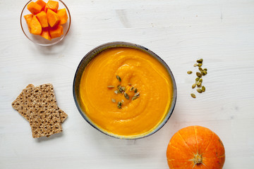 Pumpkin soup with pumpkin seeds on white wood table, flat lay