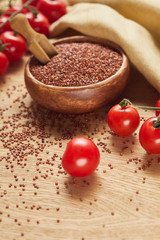 selective focus of red quinoa in wooden bowl with spatula near beige napkin and scattered tomatoes