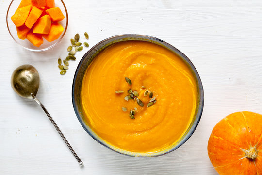 Pumpkin soup with pumpkin seeds on white wood background, top view