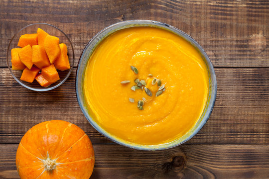 Pumpkin soup with pumpkin seeds on dark wood table, top view