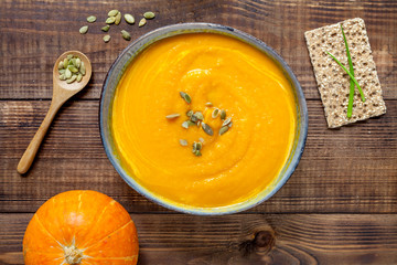 Pumpkin soup with bread rolls on wooden desk, flat lay