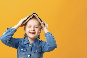 Portrait of a funny little girl on a yellow background. The student has a book on his head.