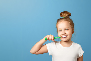 Closeup portrait of a little girl on a blue background. A child brushes his teeth with a...