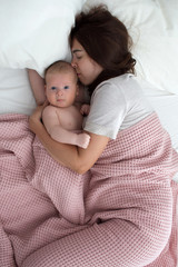 Fototapeta na wymiar A brunette woman kisses a baby. Mom with baby closeup