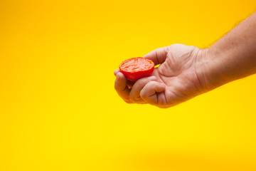 Tomate en la mano de una persona con fondo amarillo, tomate ecológico