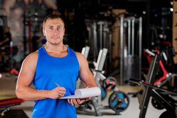 Portrait of a man, a personal trainer holding a clipboard with a training plan in the gym.