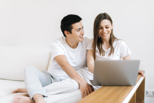 Portrait of happy young couple sitting on couch and working on laptop at home. Happy young couple is working on laptop in bright apartment.