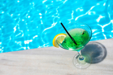 Tropical cocktail glass with lemon and straw near the swimming pool 