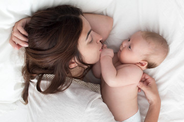 Obraz na płótnie Canvas A brunette woman kisses a baby. Mom with baby closeup