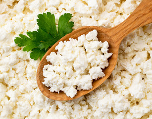 Cottage cheese in wooden spoon with parsley leaves, background. The view of the top.