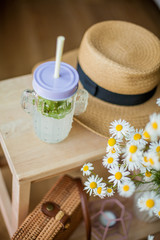 Little wicker women bag, a bouquet of daisies, lemonade with mint, wicker hat, wooden chair. Spring. Cozy.