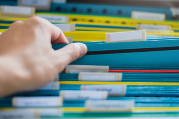 Closeup of a hand search and select a file folder from a group of file folders on shelves in an office