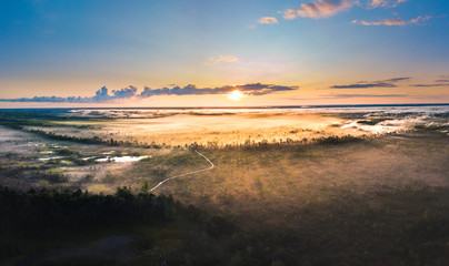  Warmly colored sunrise over a foggy swamp. Aerial view of stunning landscape at peat bog at Cenas...