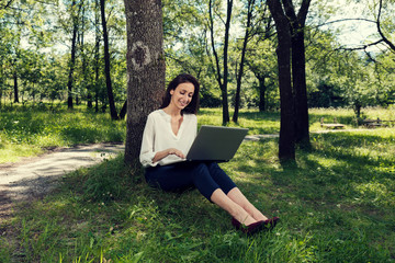 Young business woman sitting on a ground and working on her laptop in a public park and smiling Selective focus