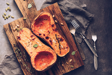 Pumpkin baked or butternut squash pumpkin with thyme on a cutting board, dark rustic background....