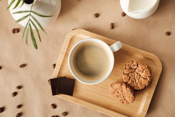 coffee with milk and oatmeal cookies and chocolate on a wooden tray