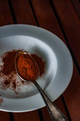 RED PEPPER IN METAL SPOON ON WHITE PLATE AND WOODEN TABLE