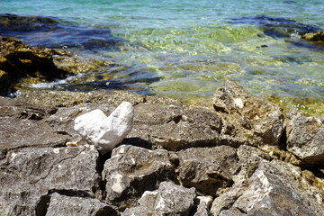 Rocks by the sea coast and one heart shaped pebble in front of the blue sea surface