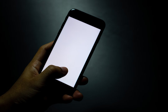silhouette hand holding and touching a mobile phone with blank wihte screen in the dark darkness against dark blue background