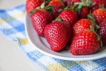Fresh strawberries on a white plate on a checkered tablecloth on a wooden table, copy space. Strawberry background. Sweet, ripe strawberries. Harvest of organic local  strawberries. Healthy food.