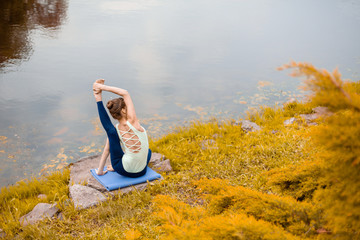 Slim brunette girl goes in for sports and performs yoga poses in the fall in nature by the lake
