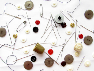 A set of needles, thimbles, buttons, pins, threads of black and red colors lying on a bright white background.