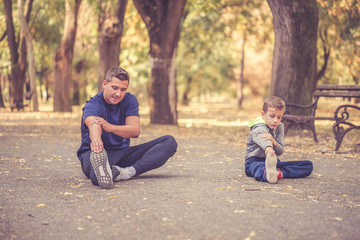 Fototapeta na wymiar Little boy and his father doing stretching exercise together in the park