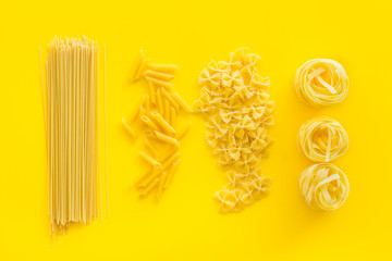 Uncooked pasta for italian food on yellow table background top view