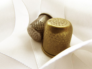 Two thimble bronze and silver on the background of white light satin ribbon.