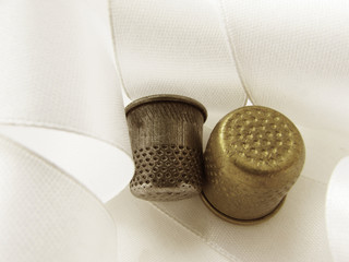 Two thimble bronze and silver on the background of white light satin ribbon.