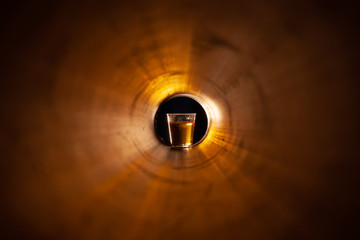 Abstraction a glass of alcohol at the end of the tunnel. Copper red yellow light. A glass with liquid on a black background at the end.