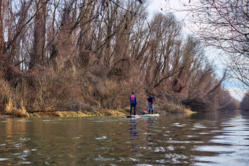 Father and son on stand up paddle boarding (SUP) paddling along the calm autumn Danube river at...
