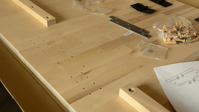 The hands of a Caucasian woman place a black metal hinge on two light wooden boards