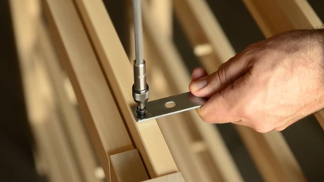 Close-up shot of a pair of screws that is fixed with an electric screwdriver on a light wooden board.