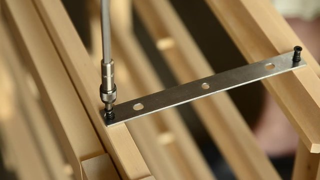 Close-up shot of a pair of screws that is fixed with an electric screwdriver on a light wooden board.