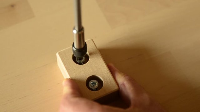 Close-up shot of a pair of screws that is fixed with an electric screwdriver on a light wooden board.