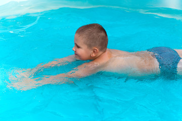 Fototapeta na wymiar little cute boy swimming in the pool with turquoise water in the summer holidays