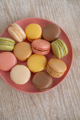 Macarons top view on pink plate against wooden background retro cute desserts. Selections of pastel color macaron.