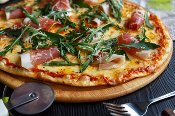 Pizza with bacon, cheese and herbs on a black wooden background
