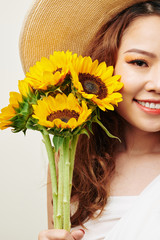 Portrait of beautiful Asian woman in hat holding sunflowers and smiling at camera