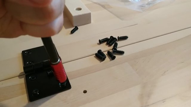 Fixing with a black metal hinge on two light wooden boards. The screwdriver is used for screwing. 25Fps